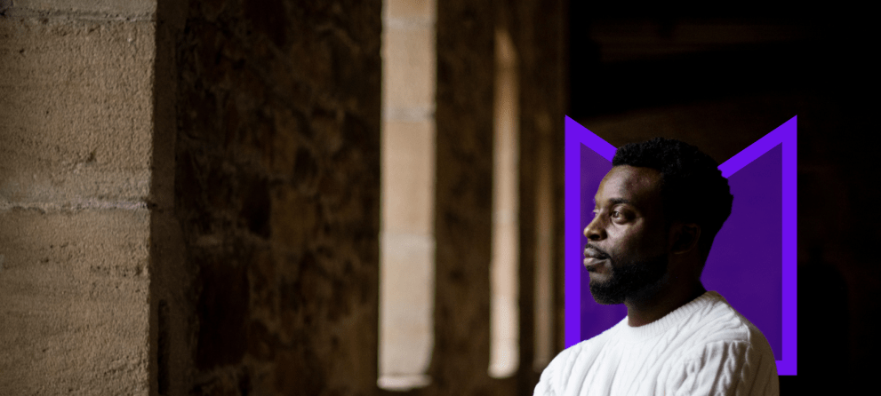 A Black man looking out of the window from a dark room.
