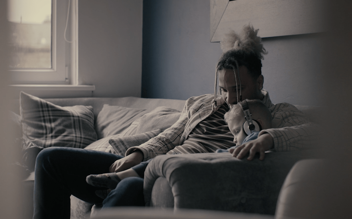 A man sitting with a boy on a sofa, the boy is wearing headphones.